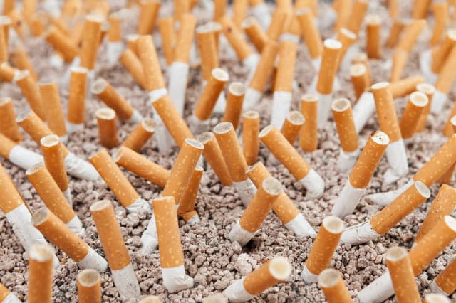 Ashtray closeup full of smoked cigarettes in the sand