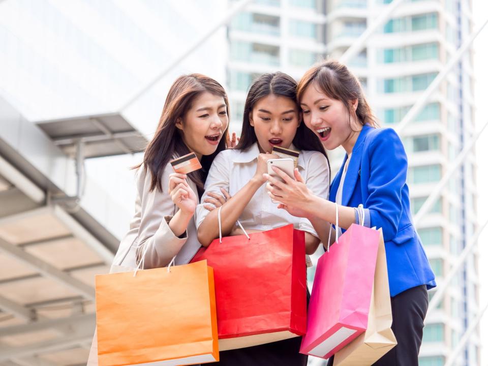 Three people hold shopping bags and look at a smartphone.