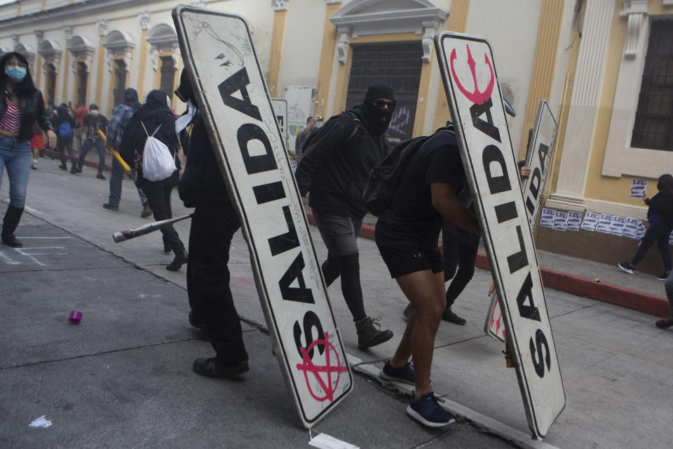 Demonstrators use transits signs as shields in front of the Congress building after protesters set a part of the building on fire, in Guatemala City, Saturday, Nov. 21, 2020. Hundreds of protesters were protesting in various parts of the country Saturday against Guatemalan President Alejandro Giammattei and members of Congress for the approval of the 2021 budget that reduced funds for education, health and the fight for human rights. (AP Photo/Oliver De Ros)