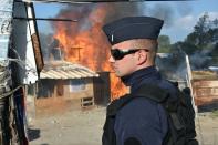 A French riot policeman keeps watch as a shack is set on fire during the demolition of the "Jungle" migrant camp in Calais, on October 25, 2016