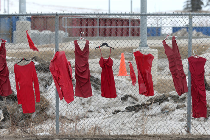 Red dresses on hangers line a fence.