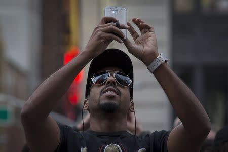 A man takes photos as he stands in front of a billboard by Revlon that takes pictures and displays them on the billboard in Times Square in the Manhattan borough of New York October 13, 2015. REUTERS/Carlo Allegri