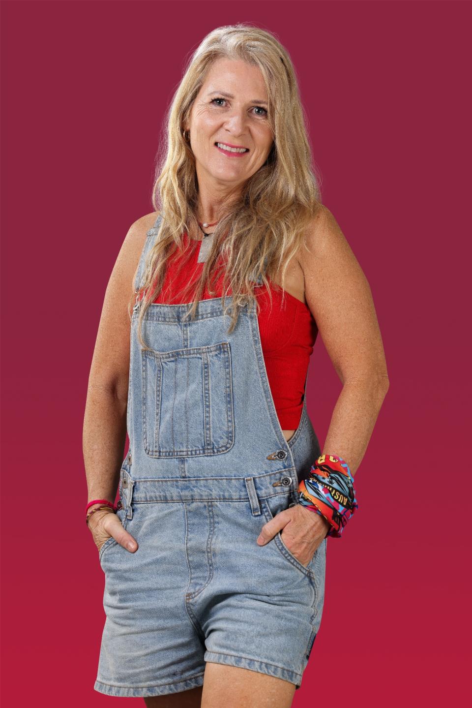 Kelli wears denim overalls and smiles at the camera.