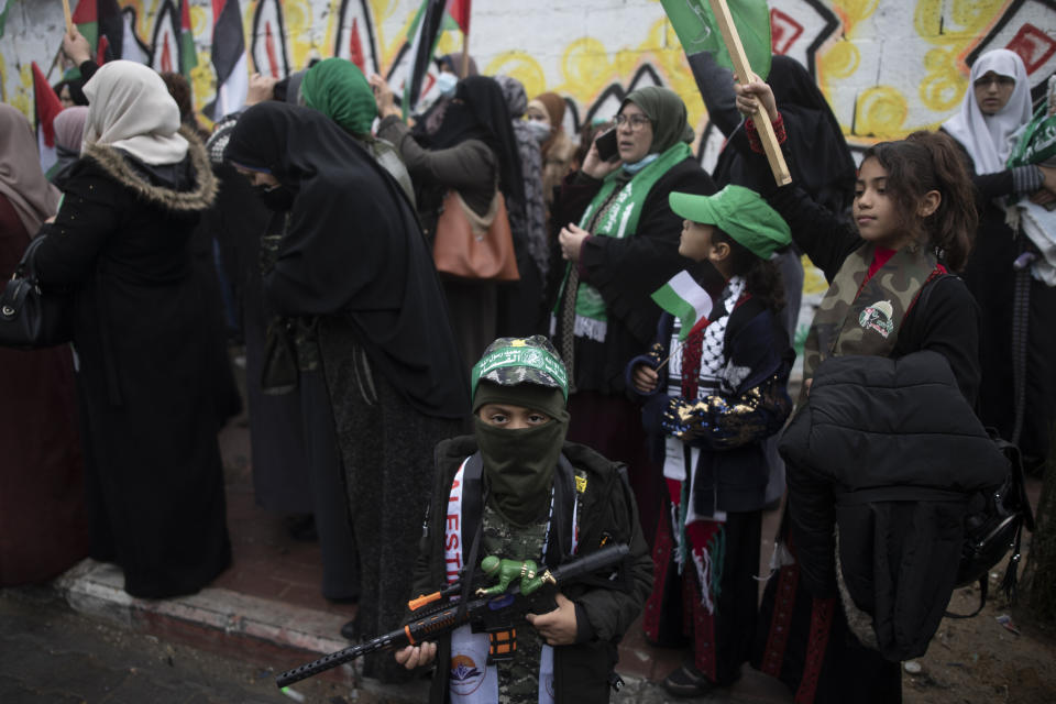 A Palestinian child wears a mask with a green head band with Arabic waiting that reads "Qassam Brigades" holds a toy gun, during a rally marking the 34th anniversary of Hamas movement's founding, in Gaza City, Friday, Dec. 17, 2021. Gaza’s Hamas rulers collect millions of dollars a month in taxes and customs at a crossing on the Egyptian border – providing a valuable source of income that helps it sustain a government and powerful armed wing. After surviving four wars and a nearly 15-year blockade, Hamas has become more resilient and Israel has been forced to accept that its sworn enemy is here to stay. (AP Photo/ Khalil Hamra)