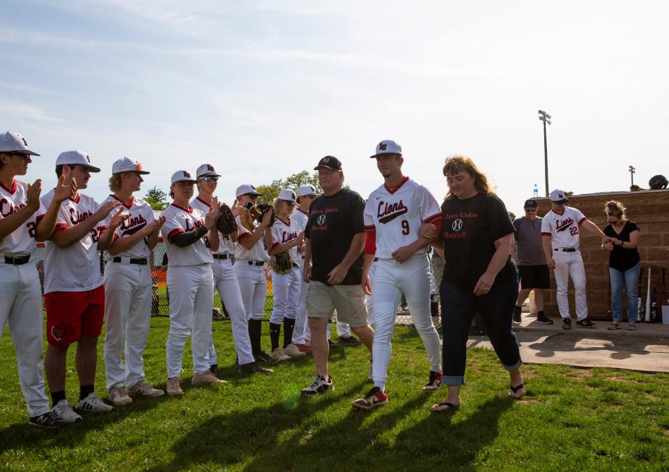 Liberty Union senior Jacob Miller walks out onto the field from the dugout with his parents to celebrate Senior Night on the baseball diamond at Liberty Union High School in Baltimore, Ohio on May 11, 2022. Jacob has been scouted for his pitching talents by Major League Baseball scouts and early projections show he will be drafted in the first round of the Major League Baseball Draft in July 2022.