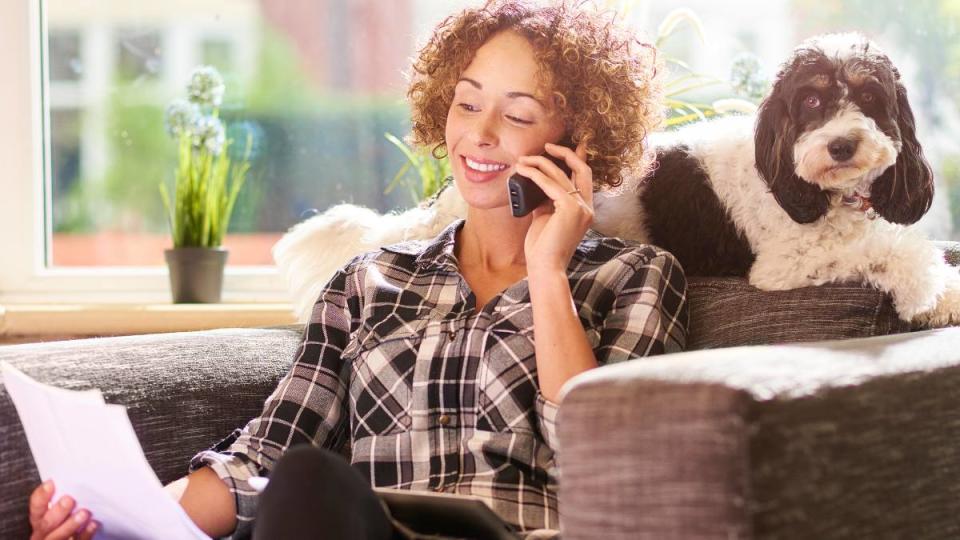 jobs working with animals: A woman sits on her chair in the living room of her home and checks a bill that she has received . She has her digital tablet on her lap ready to check against her bank account . On the back of her chair her pet dog is relaxing