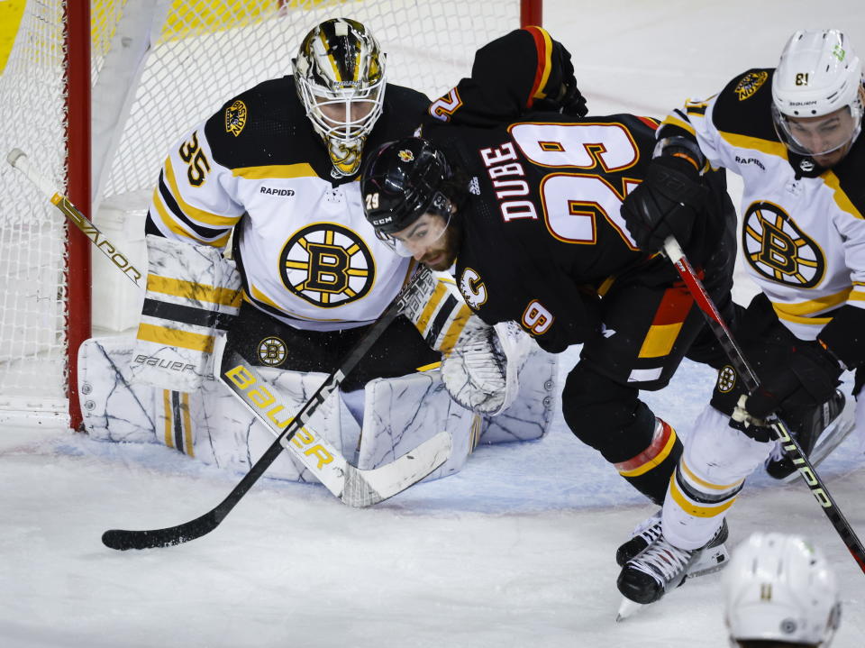 Boston Bruins defenseman Dmitry Orlov, right,, checks Calgary Flames forward Dillon Dube, center, in front of goalie Linus Ullmark during the third period of an NHL hockey game Tuesday, Feb. 28, 2023, in Calgary, Alberta. (Jeff McIntosh/The Canadian Press via AP)