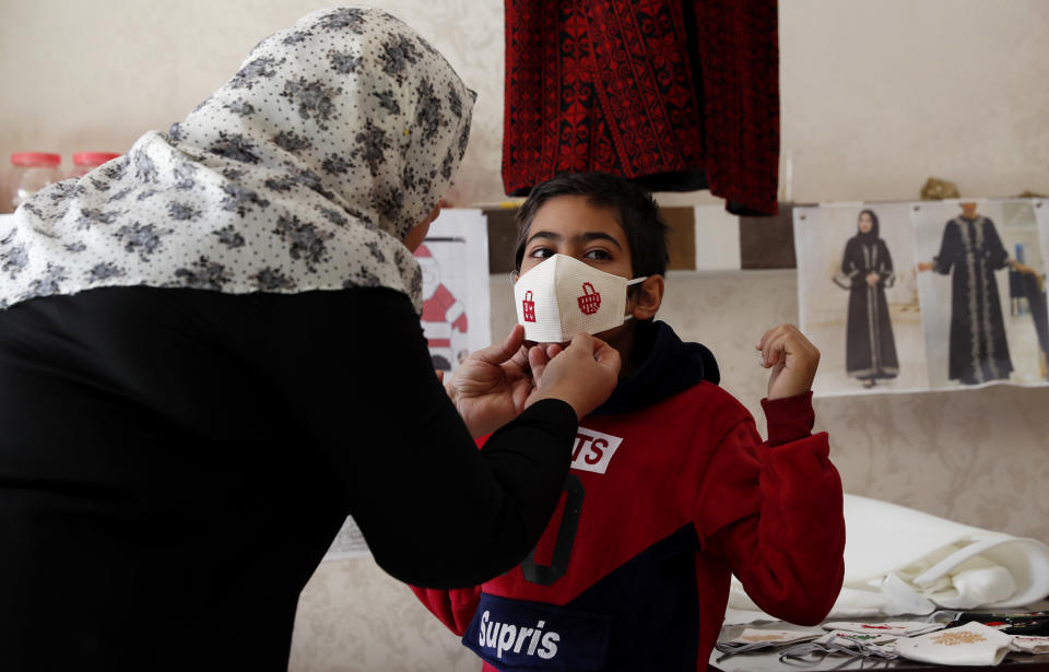 Suhad Saidam, adjusts one of her face masks on a youth at her sewing workshop in Gaza City, Monday, Dec. 14, 2020. In the blockaded Gaza Strip, the Christmas season is giving a boost to Saidam's business that produces pandemic face masks decorated with holiday symbols. They also have provided a small boost several dozen families in a Palestinian enclave run by the Islamic militant Hamas group. (AP Photo/Adel Hana)