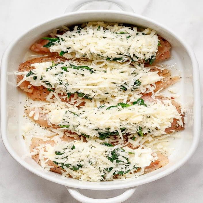 Chicken topped with spinach and cheese in a baking dish.