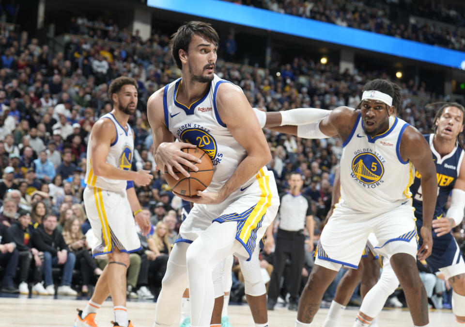 Golden State Warriors forward Dario Saric, center, pulls in a loose ball as Denver Nuggets forward Michael Porter Jr., left, jostles for position with Golden State Warriors forward Kevon Looney, behind, during the first half of an NBA basketball game Wednesday, Nov. 8, 2023, in Denver. (AP Photo/David Zalubowski)