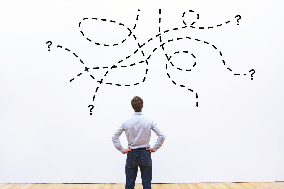 Man with hands on hips looking at a complicated drawing of lines on a wall.