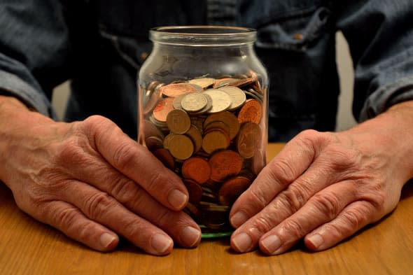 A persons hands are seen holding a money savings jar full of coins...