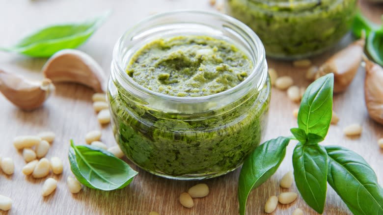 Pesto in glass jar surrounded by basil 