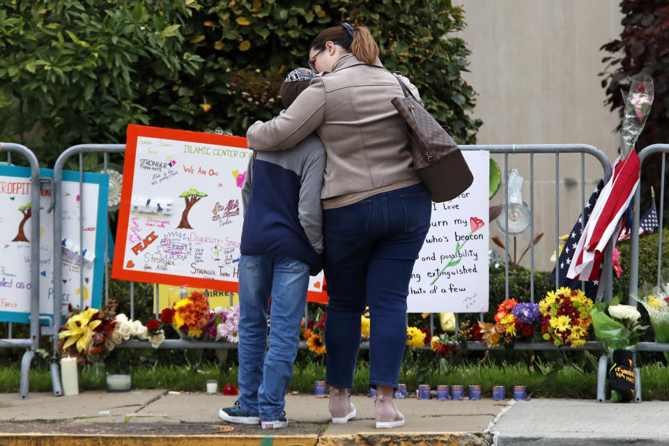 A mother hugs her son in front of a memorial at the Tree of Life synagogue in Pittsburgh on Sunday, Oct. 27, 2019, the first anniversary of the shooting at the synagogue, that killed 11 worshippers. (AP Photo/Gene J. Puskar)