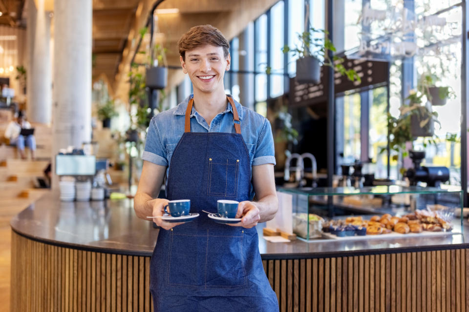 work Smiling young male barista serving two cups of coffee at office cafeteria. Young man giving coffee to customer at cafe.