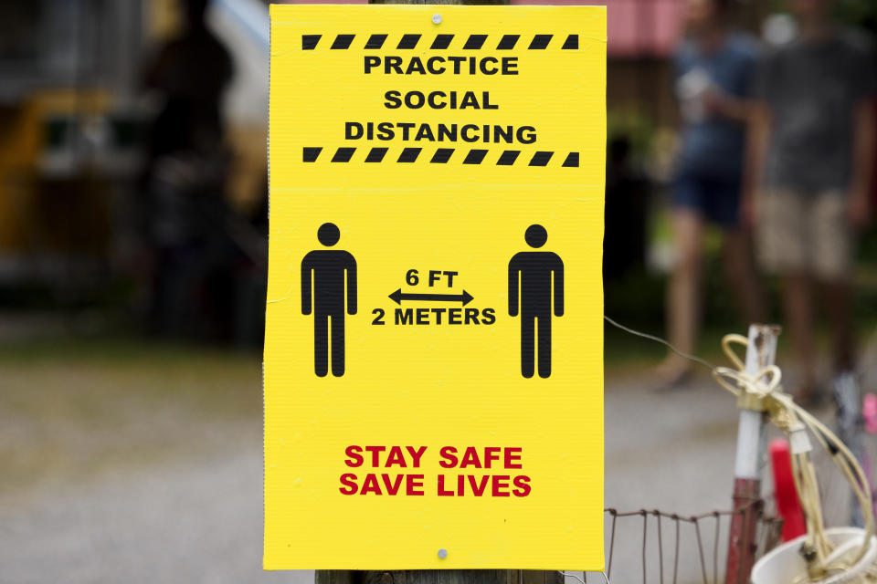 A sign encouraging social distancing is seen during the "World's Longest Yard Sale," Sunday, Aug. 9, 2020, in Dunlap, Tenn. The six-state yard sale, which was held despite concerns over the coronavirus pandemic, started Thursday and ended Sunday, and stretched from Alabama to Michigan. (C.B. Schmelter/Chattanooga Times Free Press via AP)