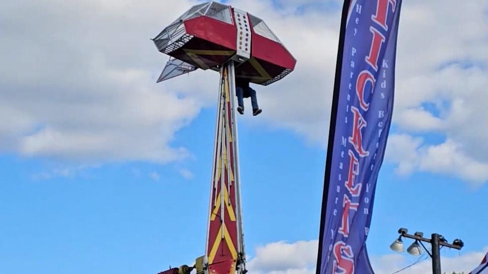 A ride operator dangles 30 feet from the ground at the annual Groves Pecan Festival in Groves, Texas after a gust of wind launched a carnival ride car into the air before the passenger could be properly secured on Oct. 15, 2023.