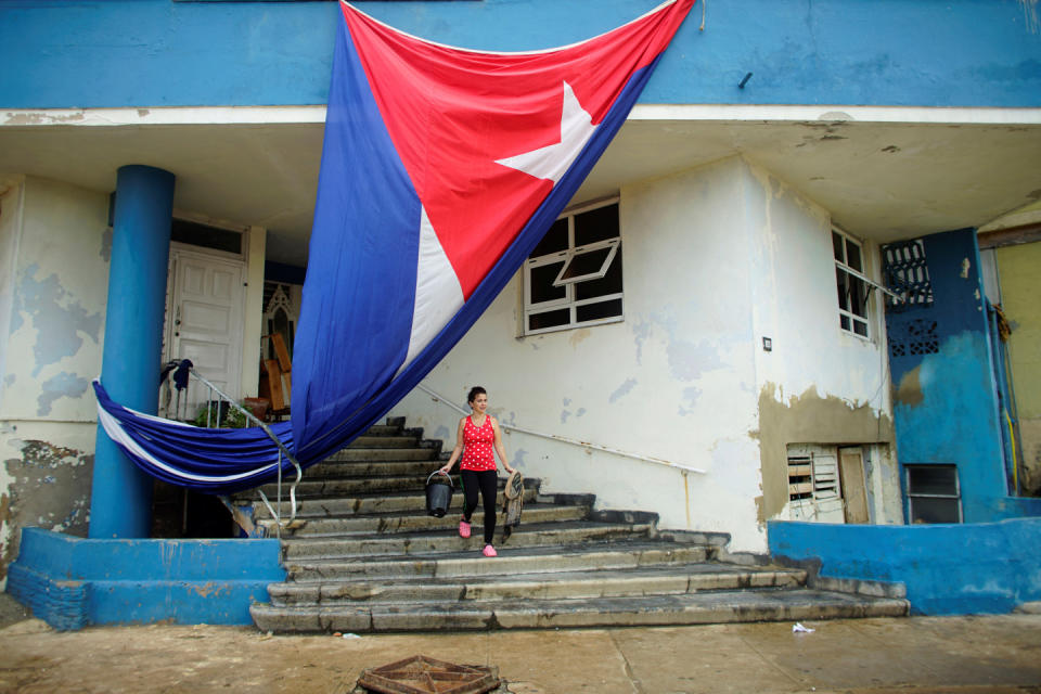 A woman cleans the entrance of a building next to a Cuban flag hung up to dry after Hurricane Irma caused flooding and a blackout, in Havana, Cuba September 11, 2017. REUTERS/Alexandre Meneghini