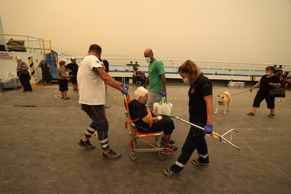 An elderly woman helped by paramedics, disembarks from a ferry which accommodated people, during a wildfire at Pefki village on Evia island, about 189 kilometers (118 miles) north of Athens, Greece, Monday, Aug. 9, 2021. Firefighters and residents battled a massive forest fire on Greece's second largest island for a seventh day Monday, fighting to save what they can from flames that have decimated vast tracts of pristine forest, destroyed homes and businesses and sent thousands fleeing. (AP Photo/Petros Karadjias)