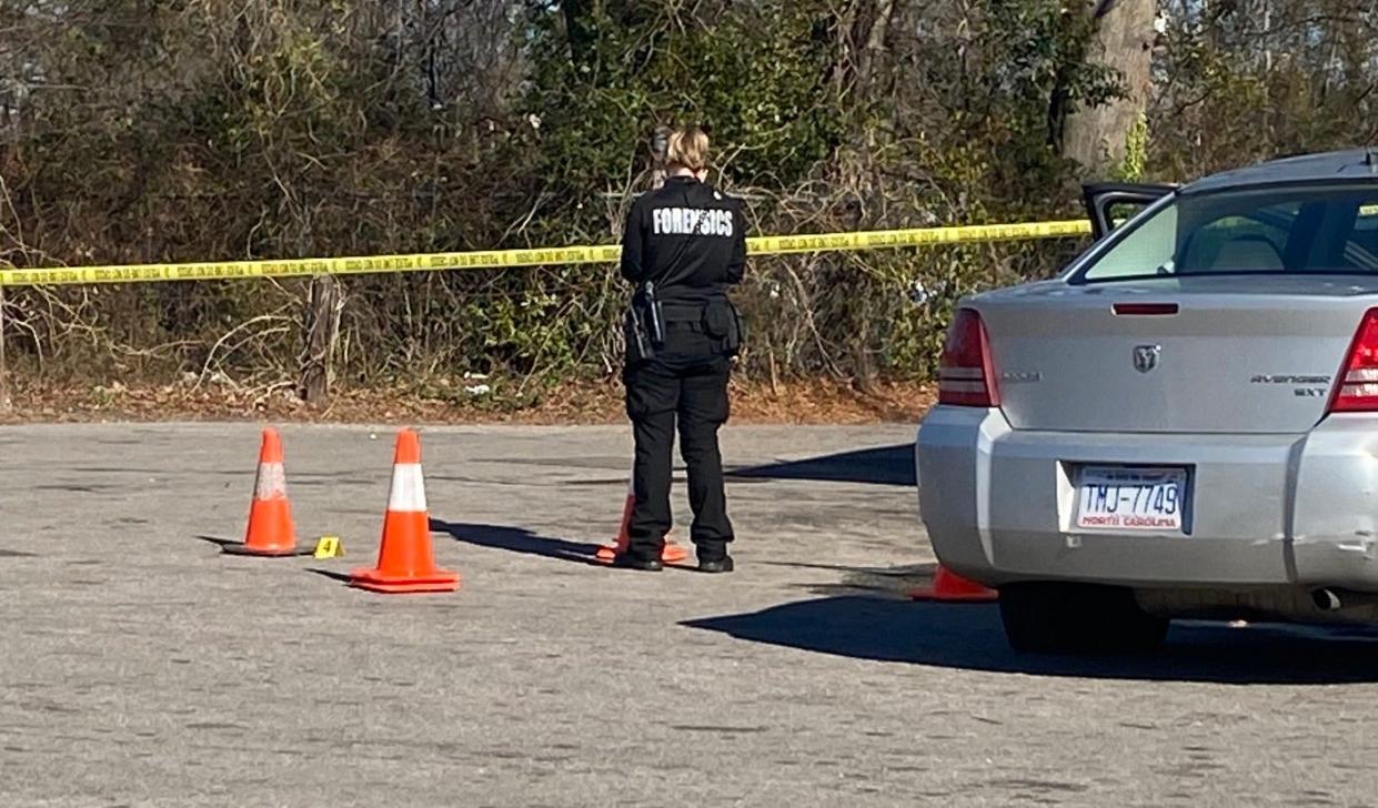 A Fayetteville Police Department forensics technician stands near evidence markers in the parking lot of the Cumberland Food Mart, after a woman was shot outside there Monday afternoon.