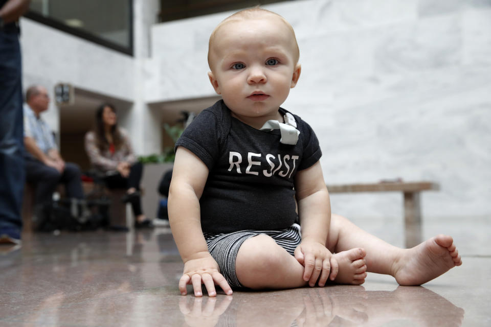 Gavin McGill, 9 months, of Washington, wears a "resist" onesie while attending a protest with his mother and brother against the separation of immigrant families, Thursday, July 26, 2018, on Capitol Hill in Washington. The Trump administration faces a court-imposed deadline Thursday to reunite thousands of children and parents who were forcibly separated at the U.S.-Mexico border, an enormous logistical task brought on by its "zero tolerance" policy on illegal entry. (AP Photo/Jacquelyn Martin)