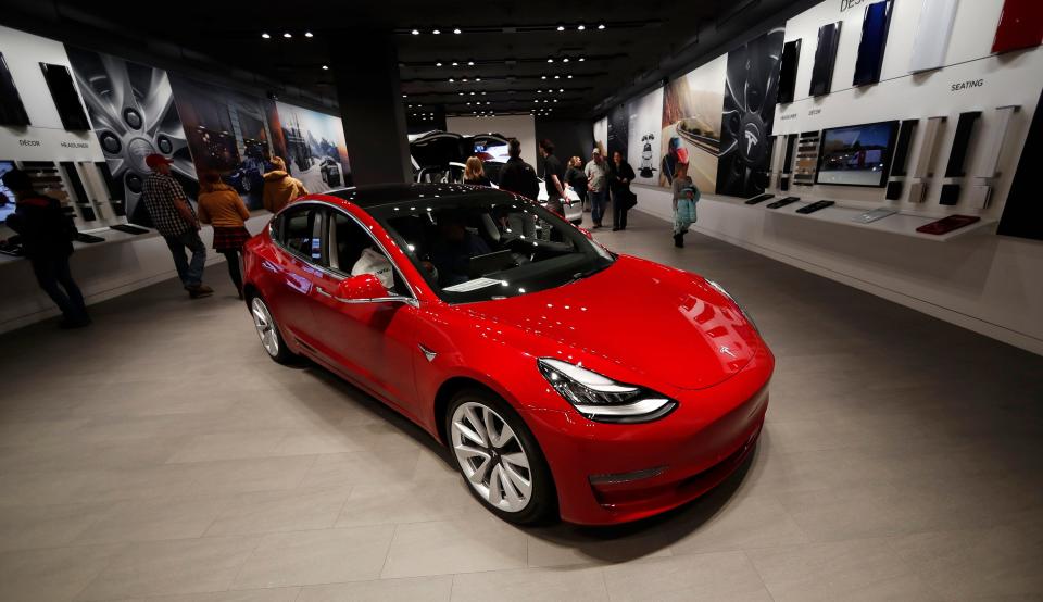 A red Tesla Model 3 on a showroom floor.