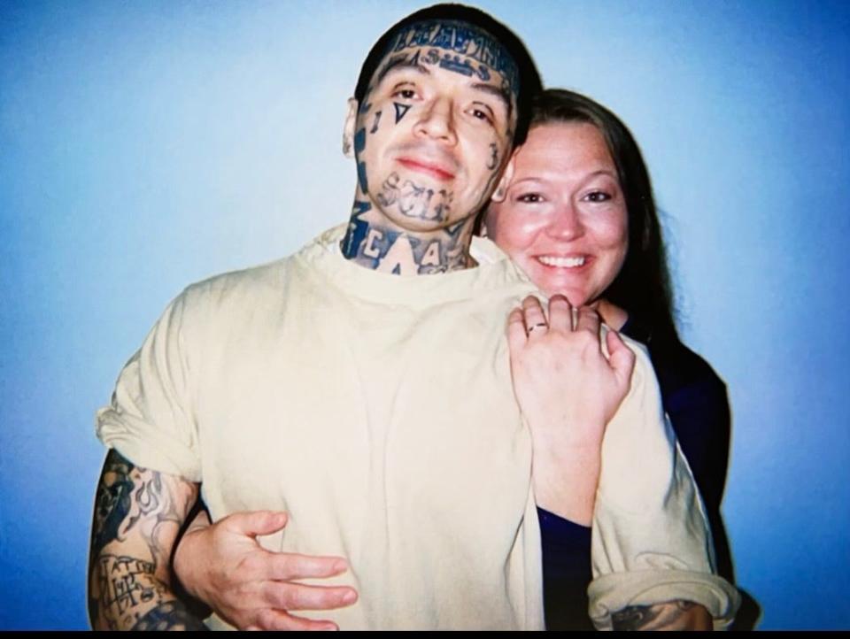 A tattooed Adrian Duran is embraced by Jamie Elliott against a plain blue backdrop.