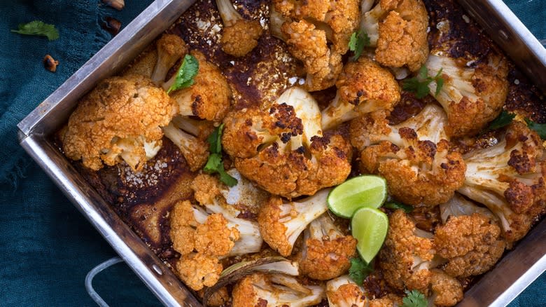 Top-down view of roasted cauliflower florets in a pan with limes