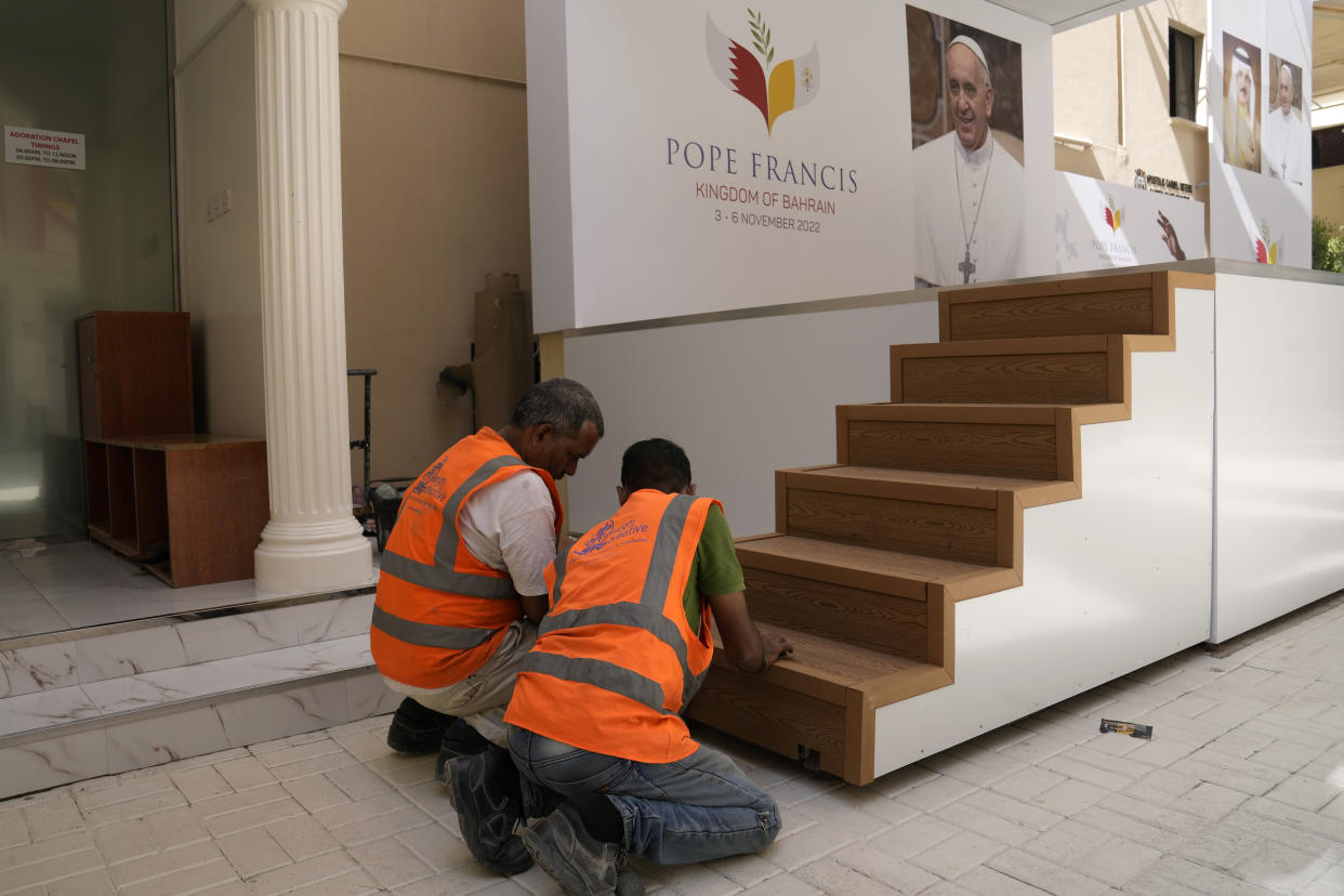 Workers adjust stairs on a podium next to a portrait of Pope Francis during preparations for the papal visit at the Sacred Heart Church in Manama, Bahrain, Wednesday, Nov. 2, 2022. Pope Francis is making a November 3-6 visit to participate in a government-sponsored conference on East-West dialogue and to minister to Bahrain's tiny Catholic community, part of his effort to pursue dialogue with the Muslim world. (AP Photo/Hussein Malla)