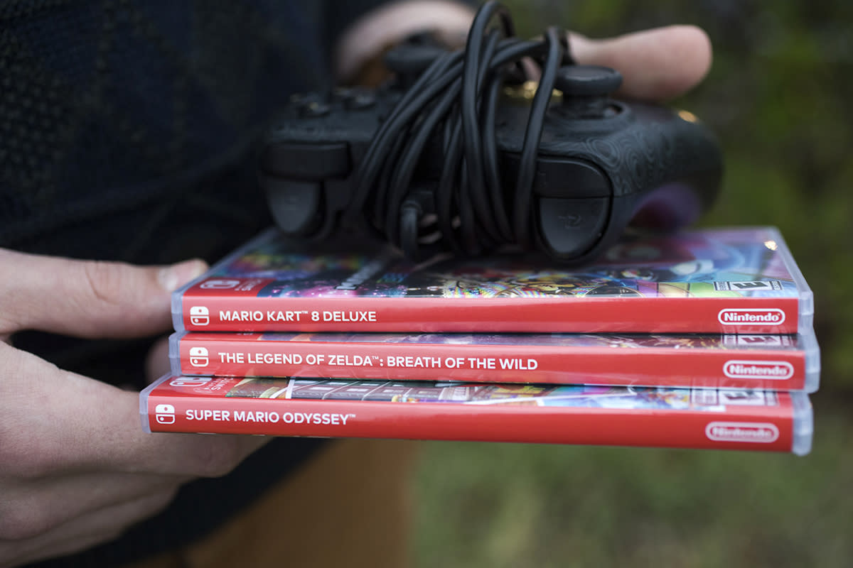 A person holds video game boxes and a controller.