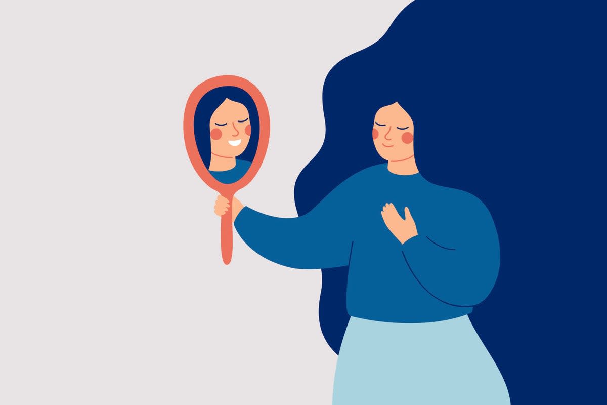 La mujer joven mira el espejo y ve su reflejo feliz. Concepto de autoaceptación y confianza.  (Ponomariova_Maria)