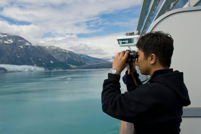 A person looking through binoculars at snowy mountains from the deck of a cruise ship.