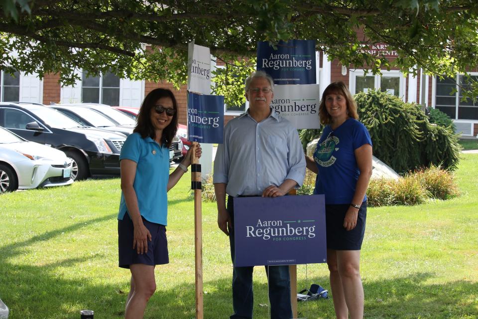 State Senator Linda Ujifusa, State Representative Michelle McGaw and Town Councilor Len Katzman hold up signs in support of CD1 candidate Aaron Regunberg in front of the St. Barnabas Church polling location.