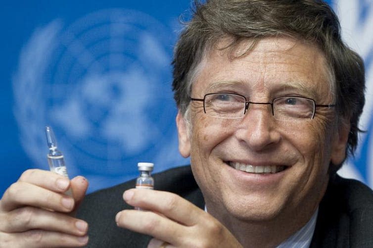 Bill Gates in front of UN logo holding a vaccine.