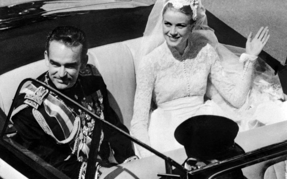 Prince Rainier III of Monaco and US actress and princess of Monaco Grace Kelly salute the crowd as they leave Saint Nicholas Cathedral after their wedding ceremony in Monaco on April 19, 1956 - Credit: AFP