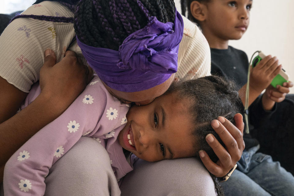 Christina Engram kisses daughter, Neveah, 6, as son, Choncey, right, 4, plays a video game at home in Oakland, Calif., on Friday Nov. 24, 2023. (AP Photo/Loren Elliott)