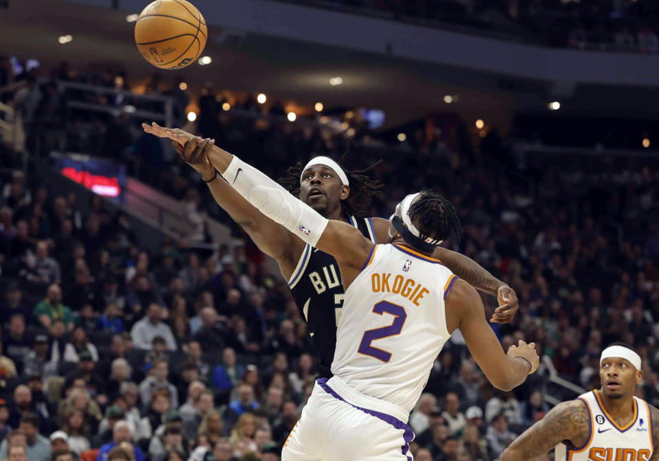 Milwaukee Bucks guard Jrue Holiday (21) reaches for a loose ball against Phoenix Suns forward Josh Okogie (2) during the first half of an NBA basketball game Sunday, Feb. 26, 2023, in Milwaukee. (AP Photo/Jeffrey Phelps)