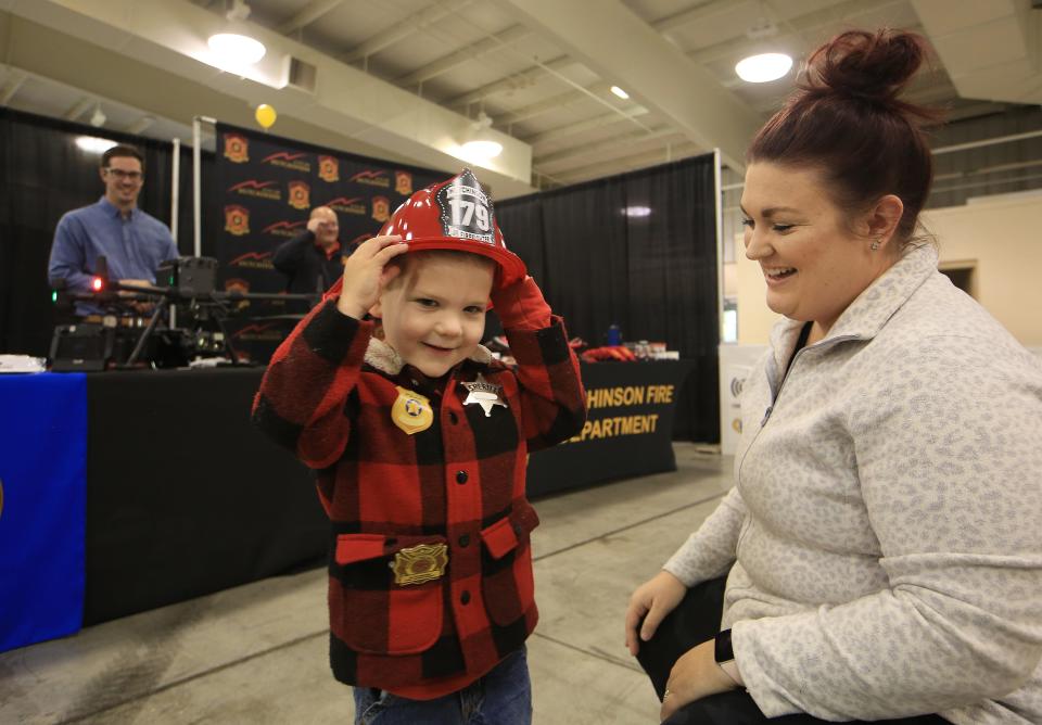 Everett Gates, 3, adjusts his firefighter hat with his mother Sophia Gates during Friday's Ignite! Business Expo, a business networking event, held on Nov. 5, 2021 in the Sunflower North and South buildings at the Kansas State Fairgrounds.