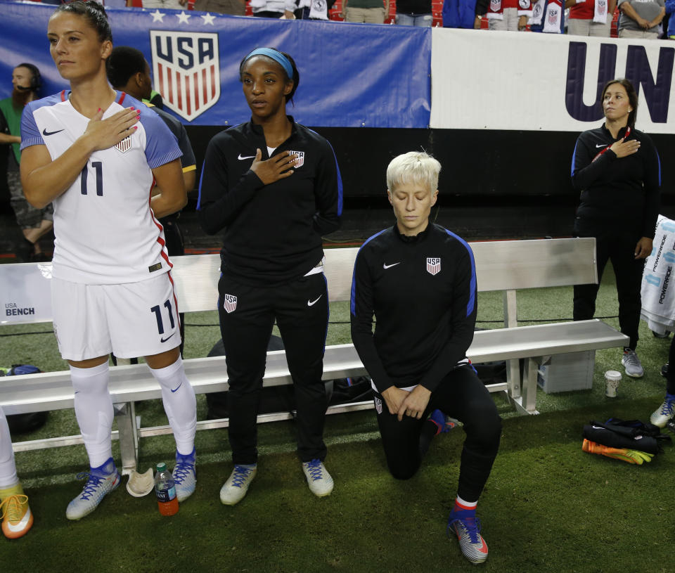 FILE - In this Sunday, Sept. 18, 2016, file photo, USA's Megan Rapinoe, right, kneels next to teammates Ali Krieger (11) and Crystal Dunn (16) as the U.S. national anthem is played before an exhibition soccer match against Netherlands, in Atlanta. The U.S. Soccer Federation has adopted a policy that says national team players "shall stand respectfully" during national anthems. The policy was approved in February 2017 but came to light on Saturday, March 4, 2017, before the U.S. women's national team played England in a SheBelieves Cup match. The policy comes after midfielder Rapinoe knelt during the anthem at a pair of national team matches in 2016. (AP Photo/John Bazemore, File)