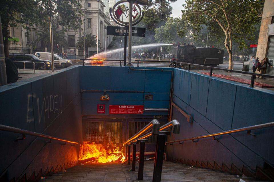 A police water cannon puts out a burning barricade near the Santa Lucia subway station during a protest against the rising cost of subway and bus fares, in Santiago, Friday, Oct. 18, 2019. (AP Photo/Esteban Felix)