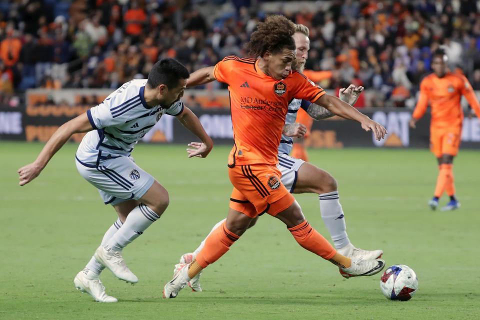 Houston Dynamo midfielder Adalberto Carrasquilla, right front, advances the ball between Sporting Kansas City midfielder Roger Espinoza, left, and forward Johnny Russell, right back, during the second half of an MLS playoff soccer match Sunday, Nov. 26, 2023, in Houston. (AP Photo/Michael Wyke)