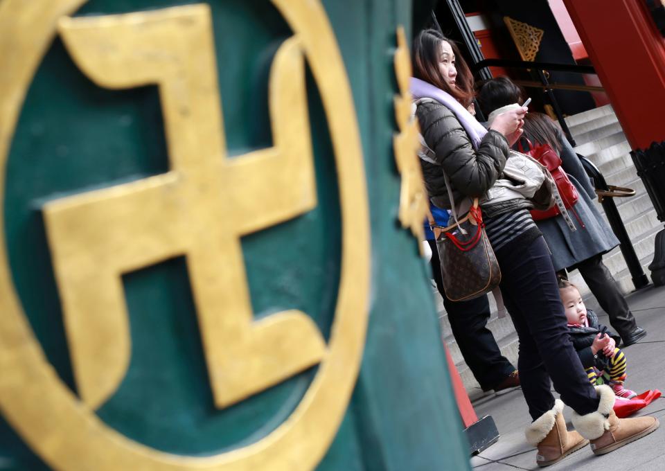 Visitors in Tokyo stand next to a religious ornament with the "manji" symbol, which comes from ancient Sanskrit and is widely used for centuries to denote Buddhist temples on maps and elsewhere. As Japan geared up to host the 2020 Olympics, catering to a surging influx of foreign visitors, the country had to wrestle with whether to continue identifying temples with a symbol often confused with a Nazi swastika.