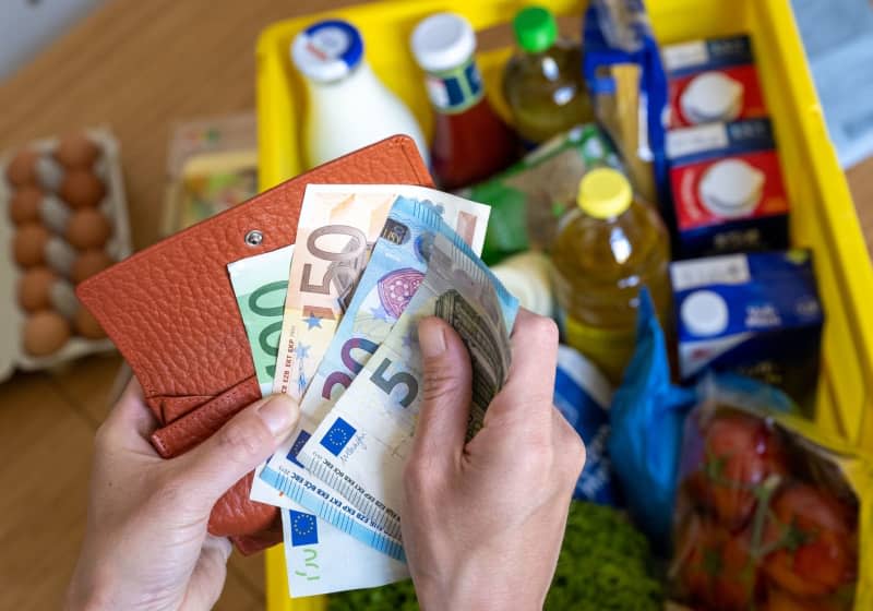 A woman counts euro banknotes while a box of groceries placed on a kitchen table. Hendrik Schmidt/Deutsche Presse-Agentur GmbH/dpa