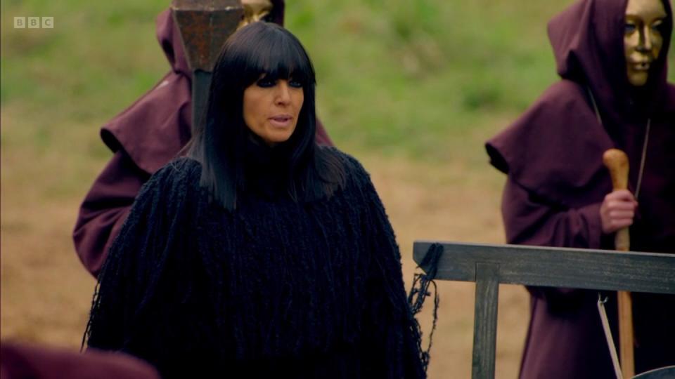 the traitors series 2 claudia winkleman in a big black cloak with some hooded and masked monk types behind her