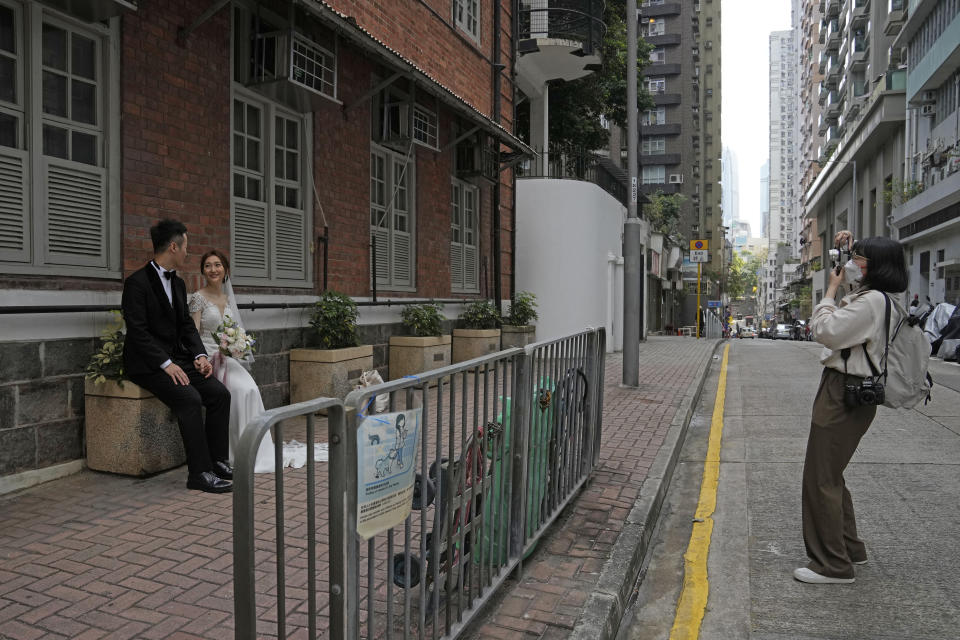 A photographer wearing a face mask takes a wedding photograph of a couple on a street in Hong Kong, Sunday, March 13, 2022. The territory's leader, Chief Executive Carrie Lam, warned the peak of the latest surge in coronavirus infections might not have passed yet. (AP Photo/Kin Cheung)