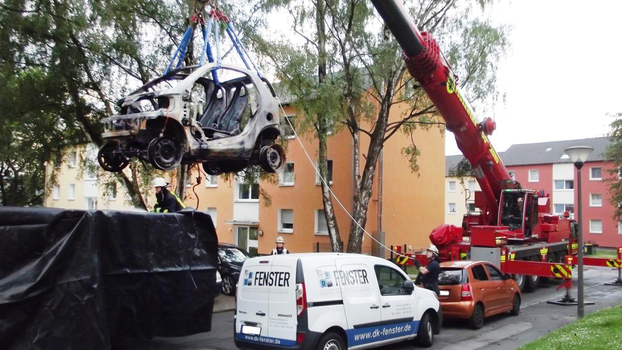 Ein Kranwagen der Dortmunder Feuerwehr hebt ein ausgebranntes E-Auto in einen Container.