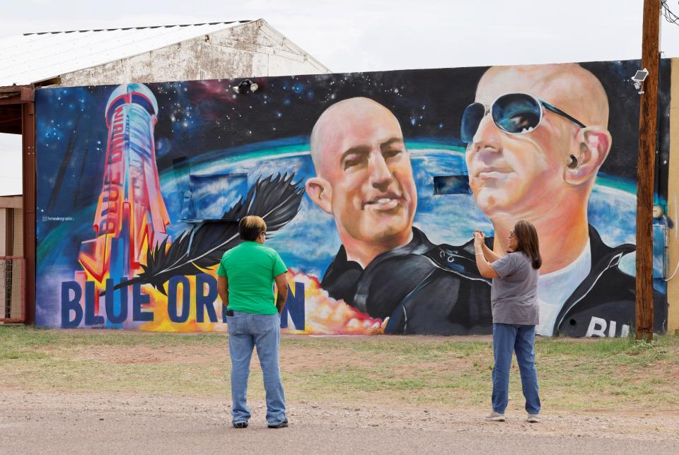 A woman photographs another person in front of a mural showing Jeff Bezos and a space launch.