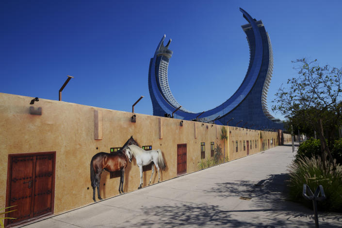 Images of horses are seen on a fence of a construction cite with the Crescent Tower Lusail in the background in Lusail downtown, Qatar, Thursday, Nov. 24, 2022. (AP Photo/Pavel Golovkin)