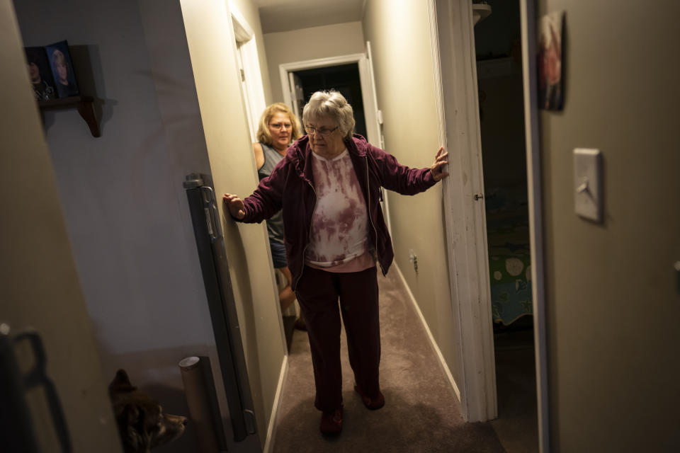 Betty Bednarowski holds the walls as she walks towards the living room while her daughter, Susan Ryder, watches from behind, Monday, Nov. 29, 2021, in Rotterdam Junction, N.Y. (AP Photo/Wong Maye-E)