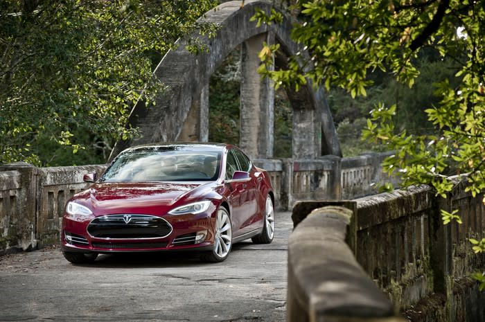 A red 2012 Tesla Model S, a large electric luxury-sports sedan, parked on a stone bridge